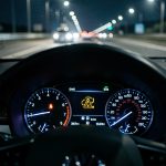 Vue réaliste du tableau de bord d’une voiture sur une autoroute de nuit, avec un voyant de dysfonctionnement moteur d’injection allumé et une ambiance cinématographique.