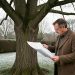 Jardin résidentiel français en hiver avec un grand arbre dénudé et un homme consultant un plan d’urbanisme vierge.